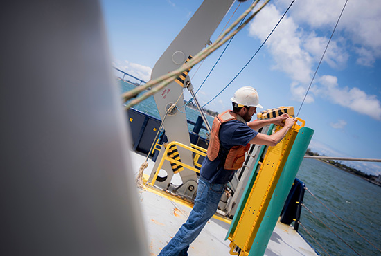 Man in safety gear works with underwater equipment on the deck of a boat.